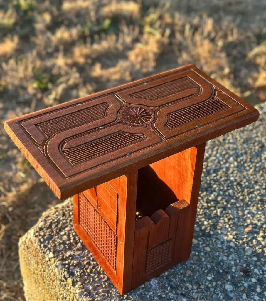 Table en bois sculptée avec un design décoratif sur le dessus, reposant sur une base solide.