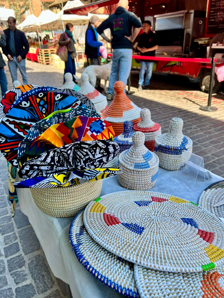 Un étal de marché présentant des paniers tissés colorés et des plats décoratifs en osier, avec des motifs vibrants, sur une table.